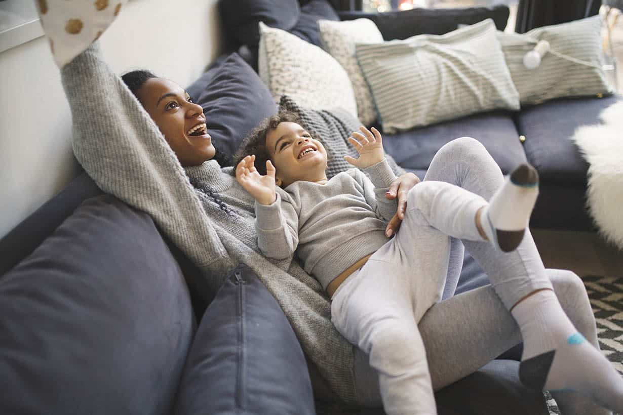 Mother and child laughing and playing on couch in living room